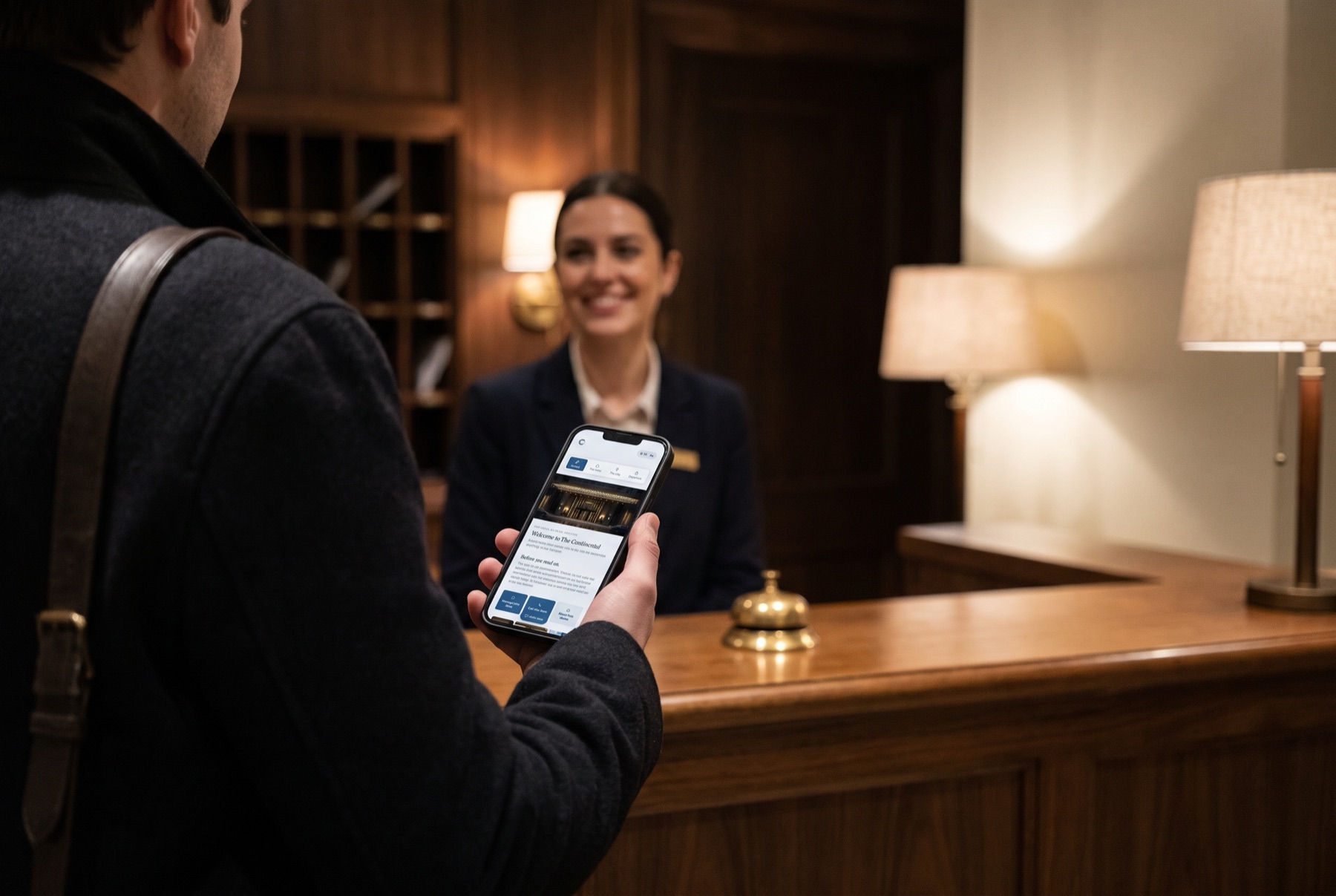 A guest at a hotel front desk in the evening, looking at The Continental’s guide on their phone